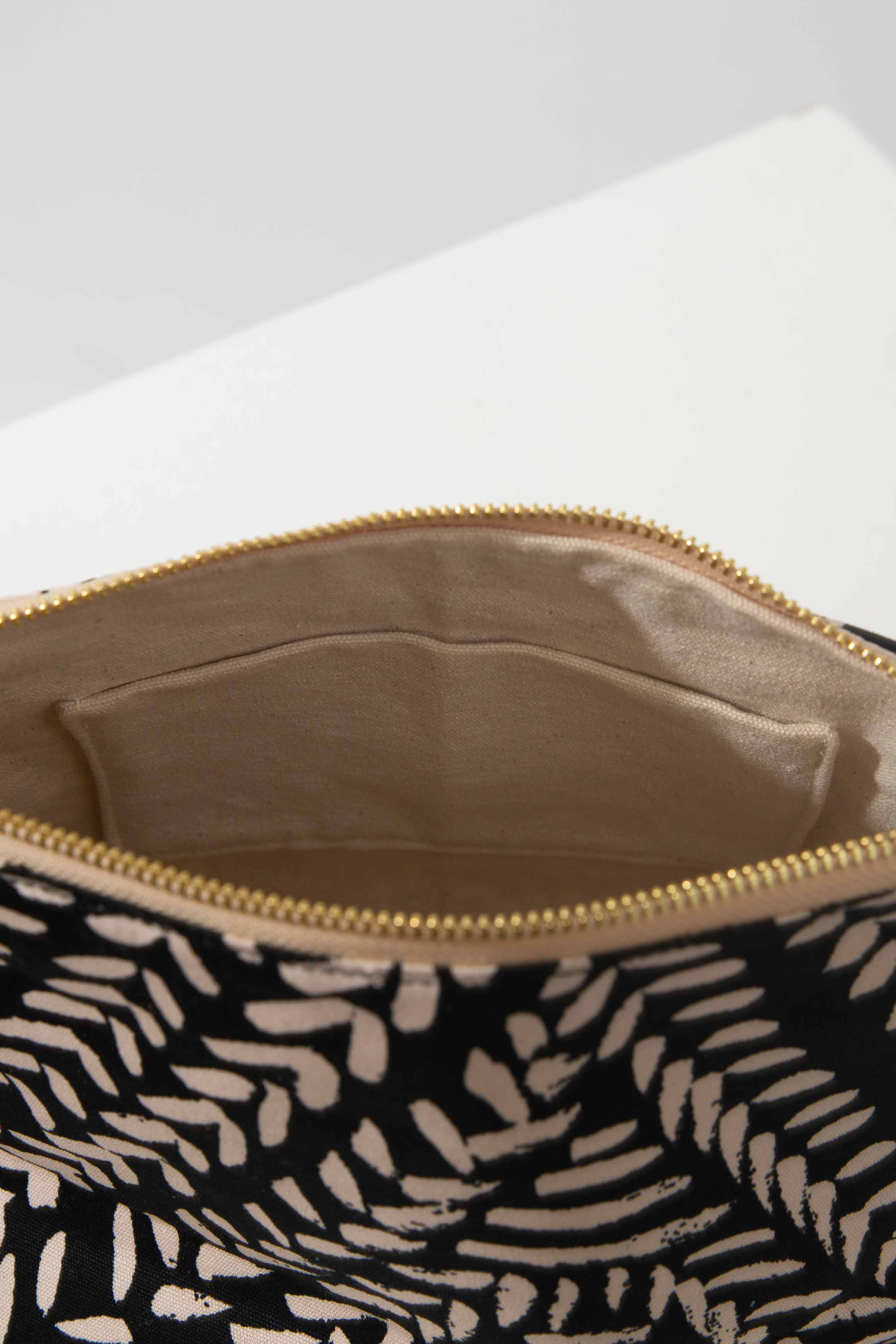 The Carryall Cosmetic Bag sits unzipped, revealing the interior back wall. It has a solid, tan fabric lining and a fabric slot pocket stitched into the back wall.