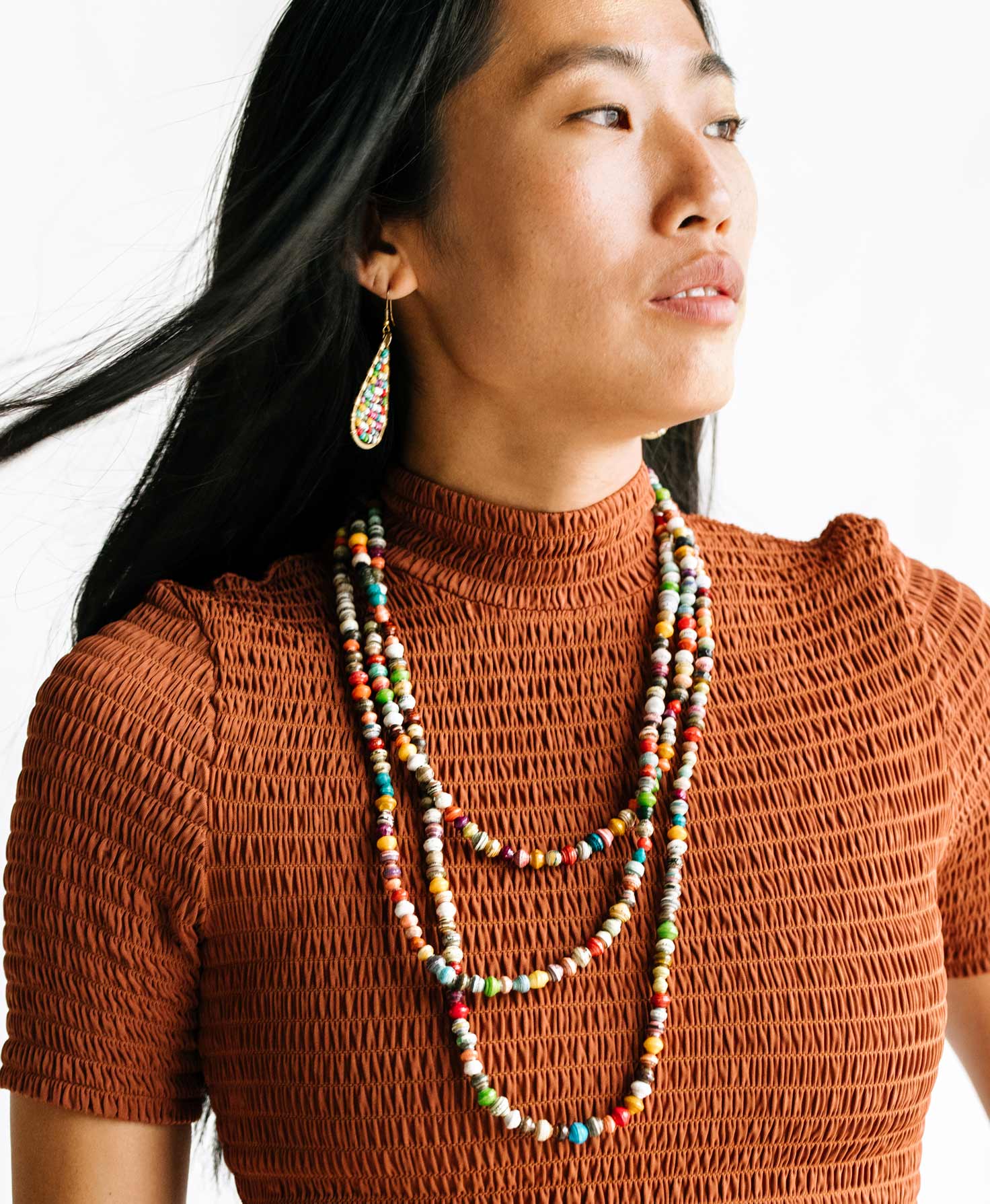A model wears the Dainty Paper Bead Necklace paired with the Paper Teardrop Earrings and Paper Play Bracelet, which also feature a bright rainbow of paper beads. 