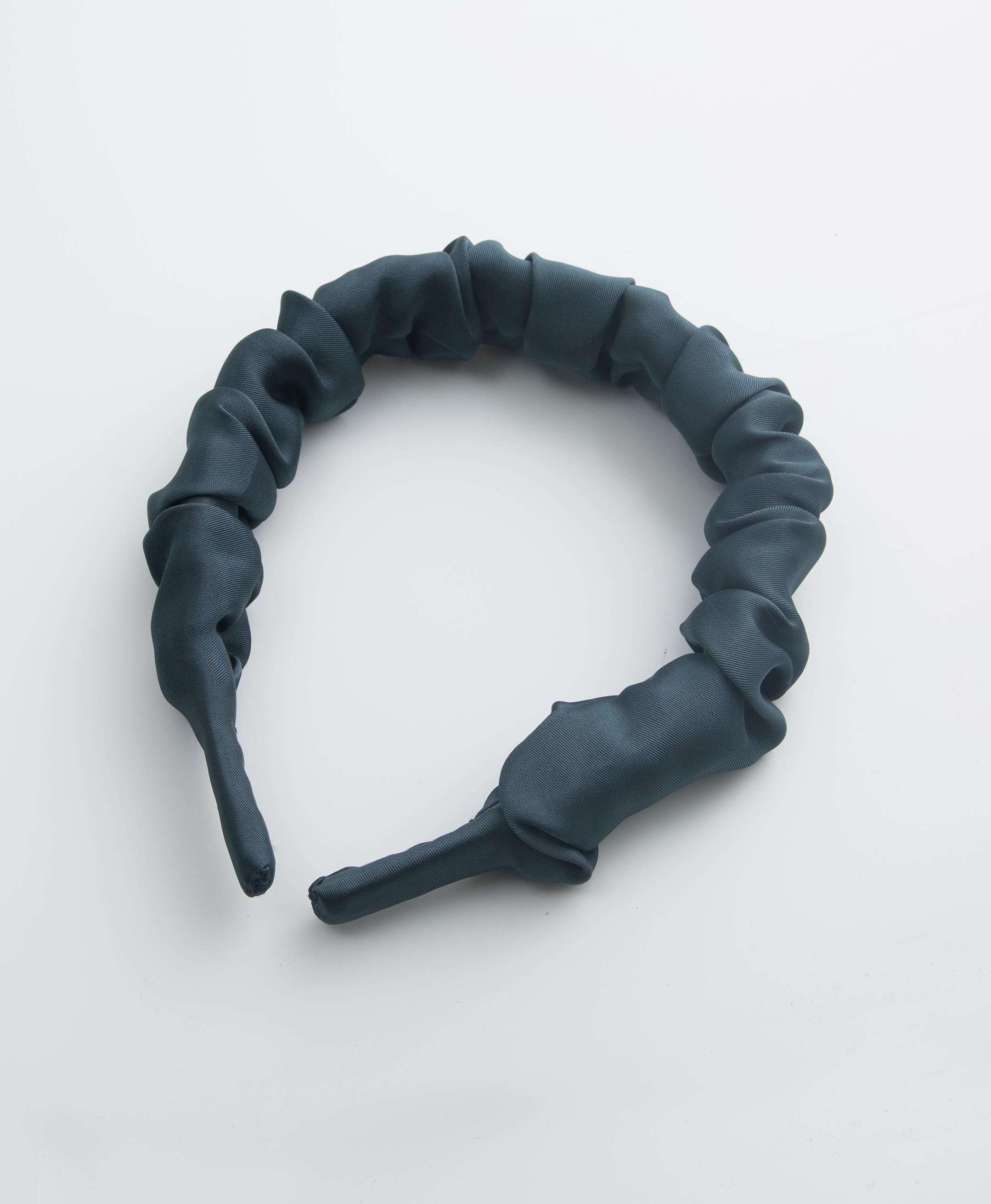 The Felicity Headband in Blue sits on a white background. It is covered in dark navy satin that is tightly pushed together to form a ruched look. 